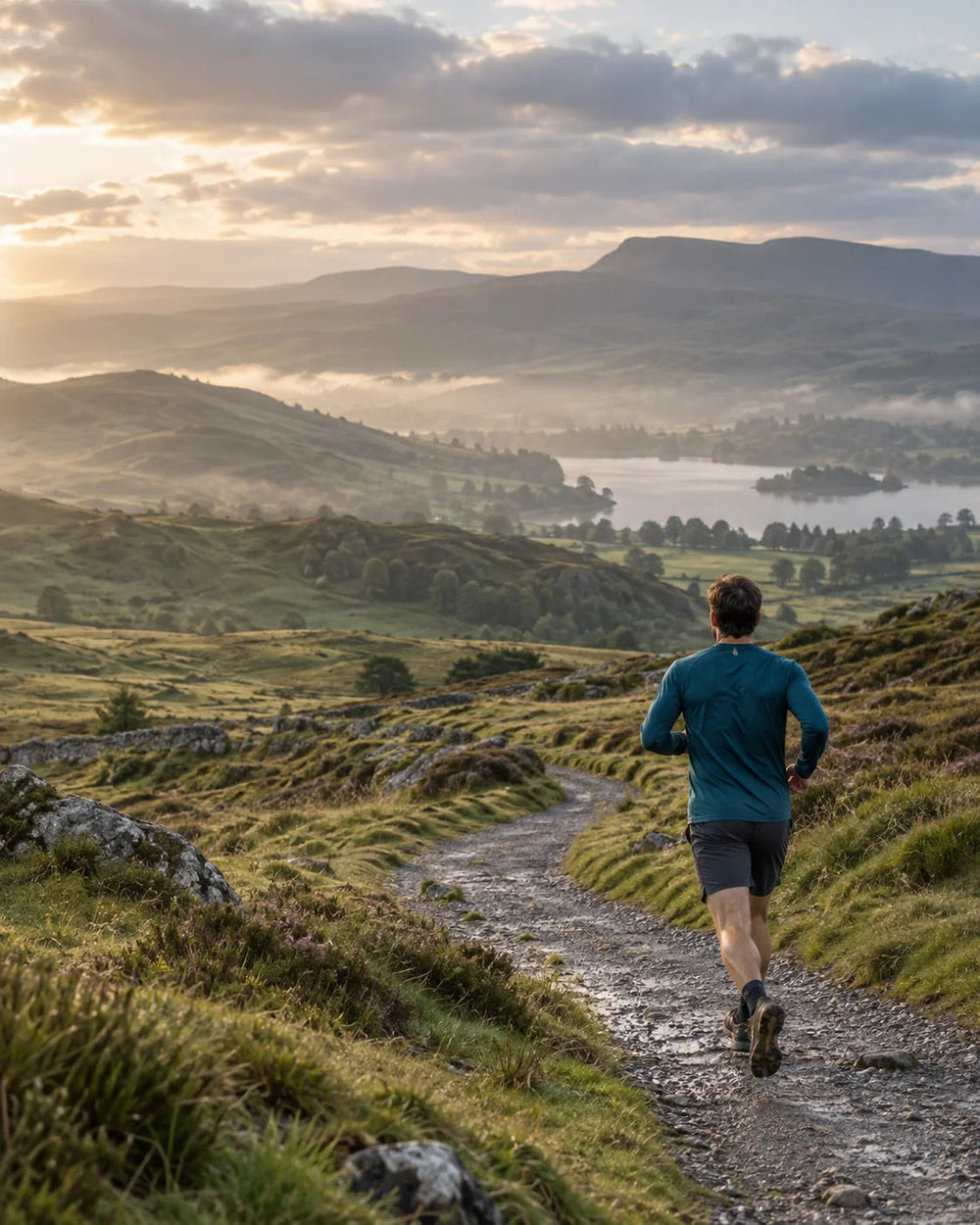 Runner following a hillside trail overlooking a lake in soft morning light