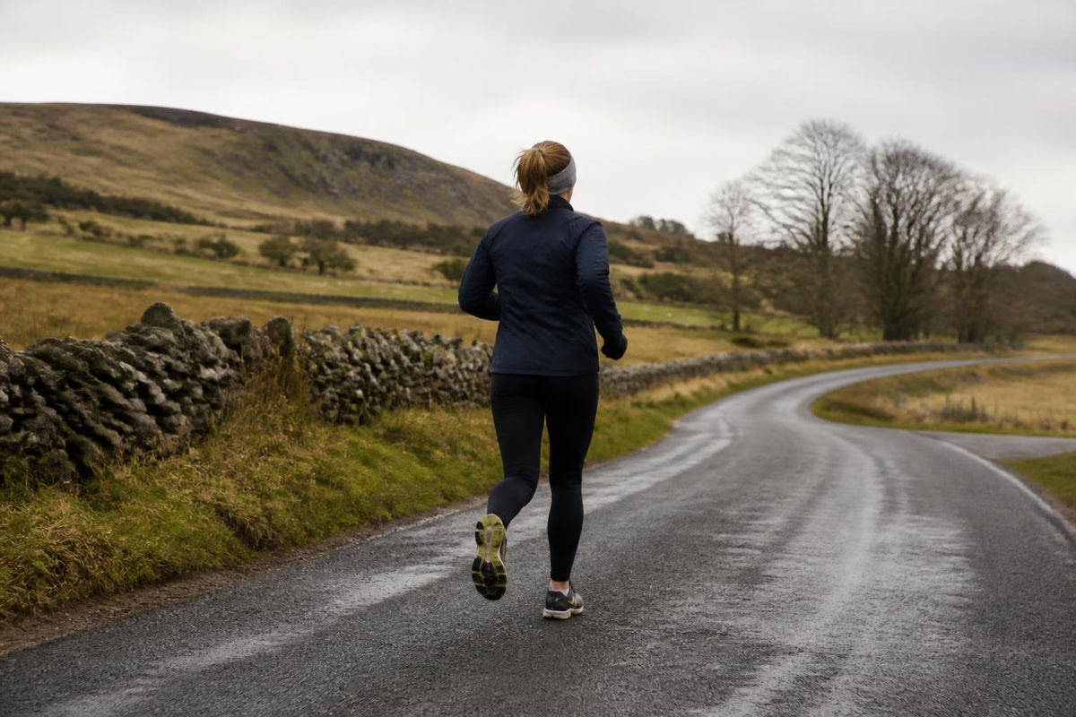A runner in high-visibility, moisture-wicking gear jogs along a misty path at dawn
