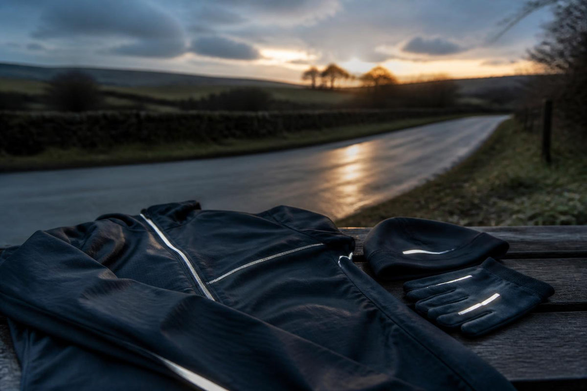 A runner wearing high-visibility gear with reflective strips stands on a dark path at dusk