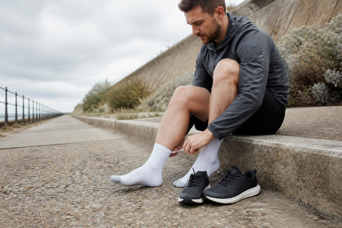 Close-up of running shoes and moisture-wicking athletic socks on a paved path in bright sunlight